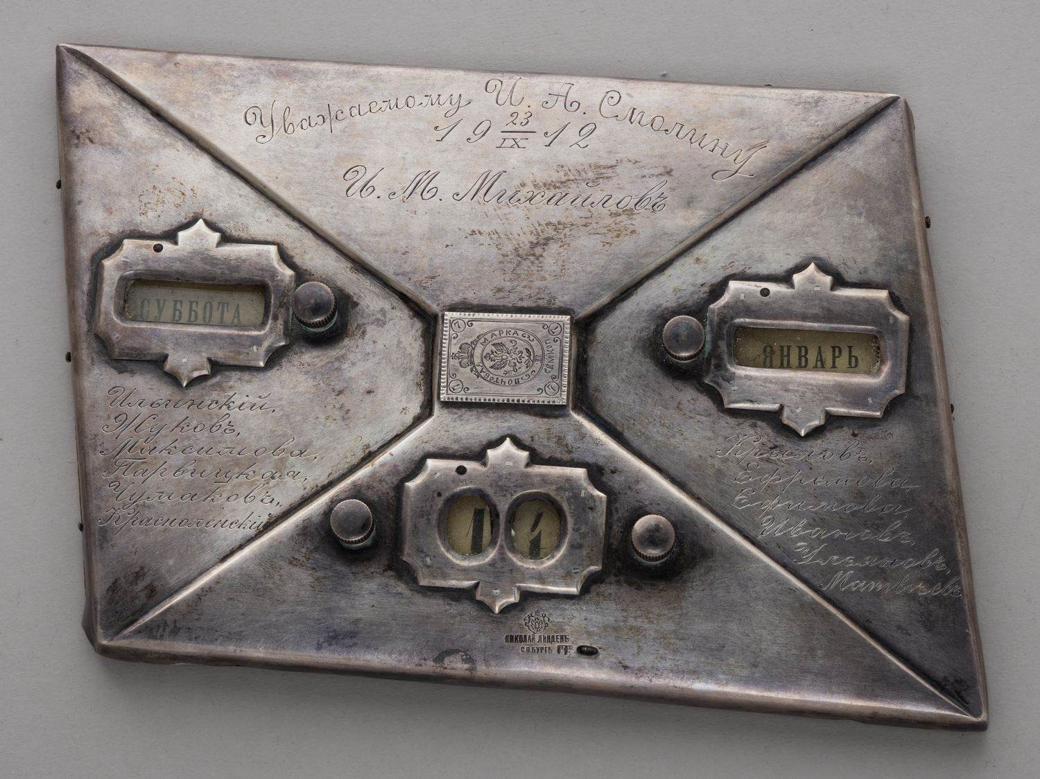 Календарь  настольный в виде почтовой марки.
Россия, Санкт-Петербург,  торгово-промышленное заведение Николая Линдена, мастер-монограммист «НК», 1912.